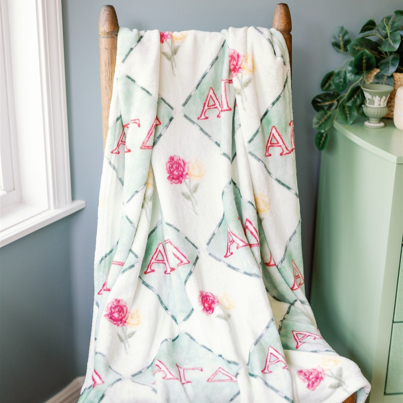 Floral Alpha Gamma Delta patterned blanket draped over a wooden chair against a blue wall.