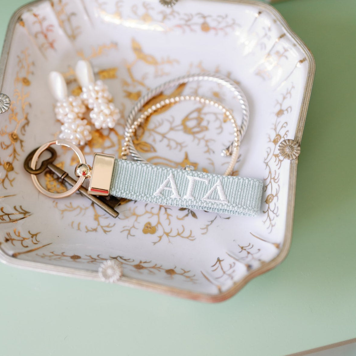 Light blue keychain with 'Alpha Gamma Delta' Greek letters on a decorative dish