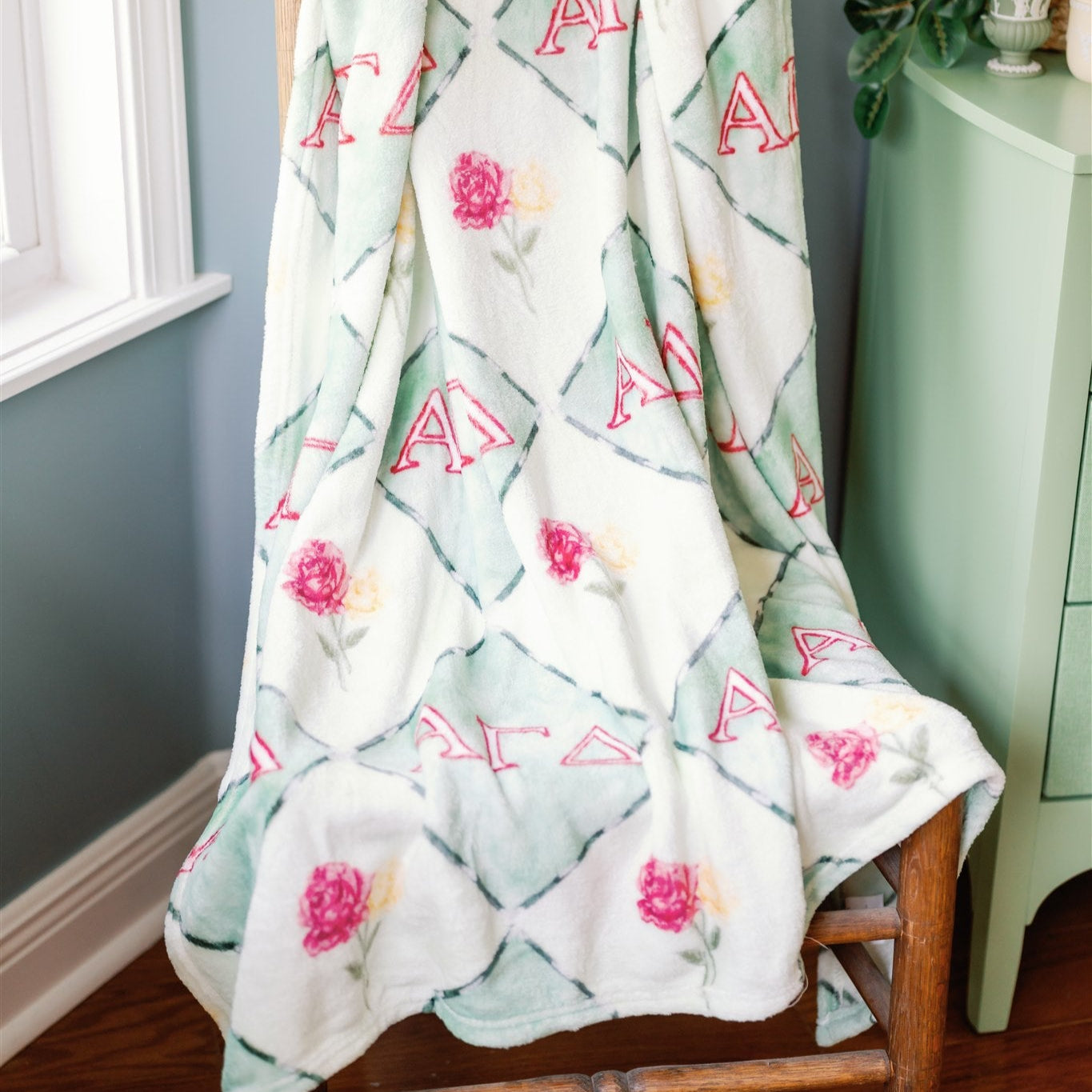 Alpha Gamma Delta patterned blanket draped over a wooden chair against a gray wall.
