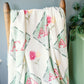 Floral patterned blanket with 'Alpha Gamma Delta' letters draped over a wooden chair against a gray wall.