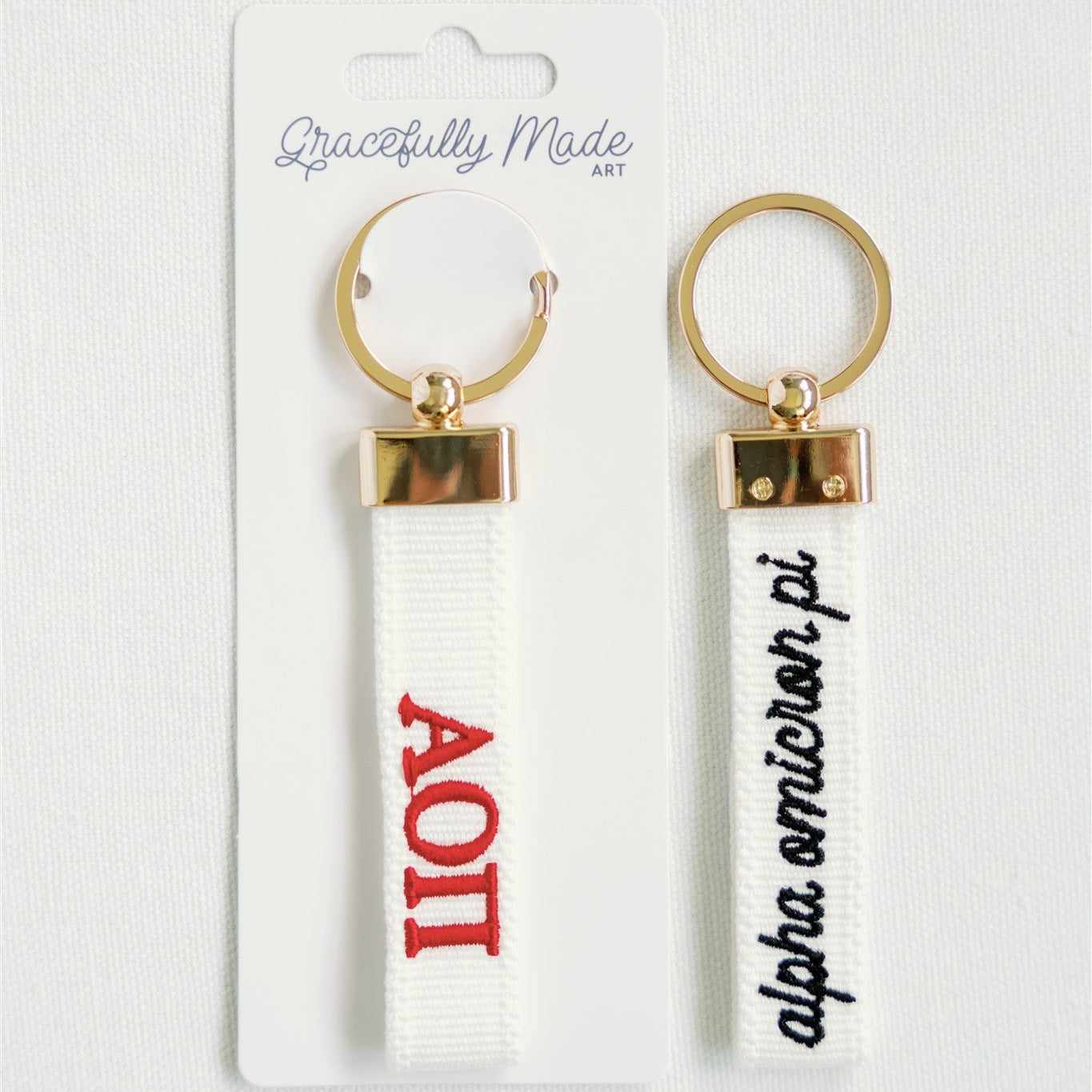 Two keychains with Alpha Omicron Pi embroidered on a card with 'Gracefully Made' branding.