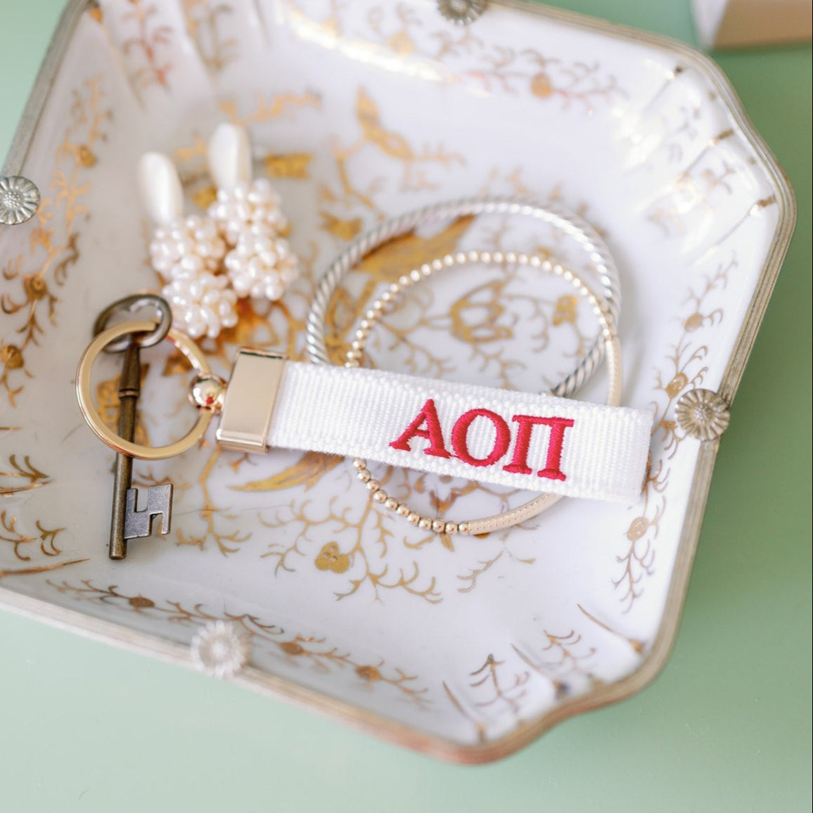 White keychain with red Alpha Omicron Pi Greek letters on a decorative dish.