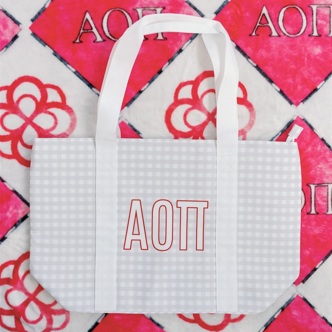 White tote bag with Alpha Gamma Pi Greek letters printed on it against a red and white patterned background. 
