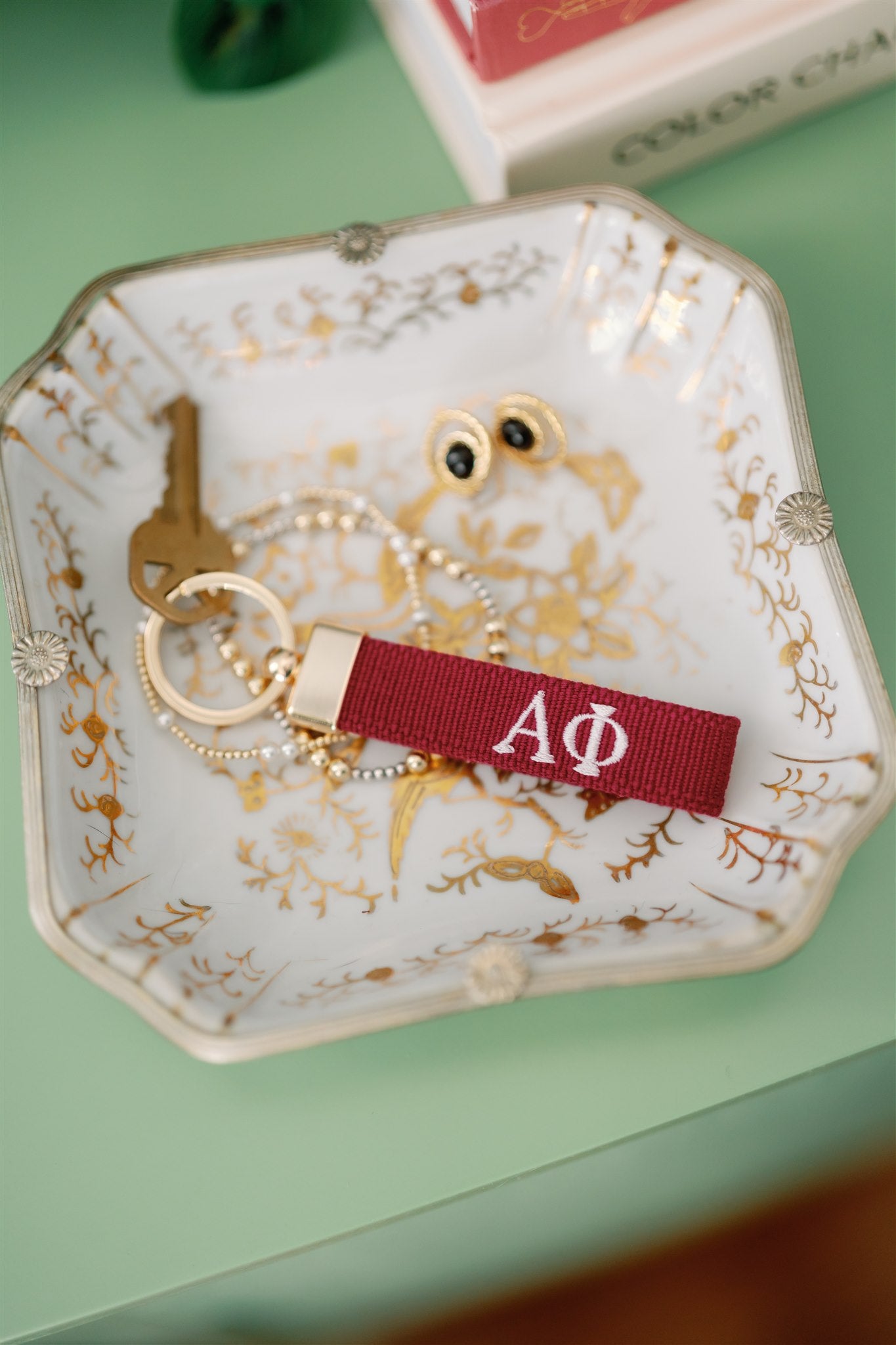 Decorative jewelry dish with a red keychain with Alpha Phi Greek letters embroidered on it.