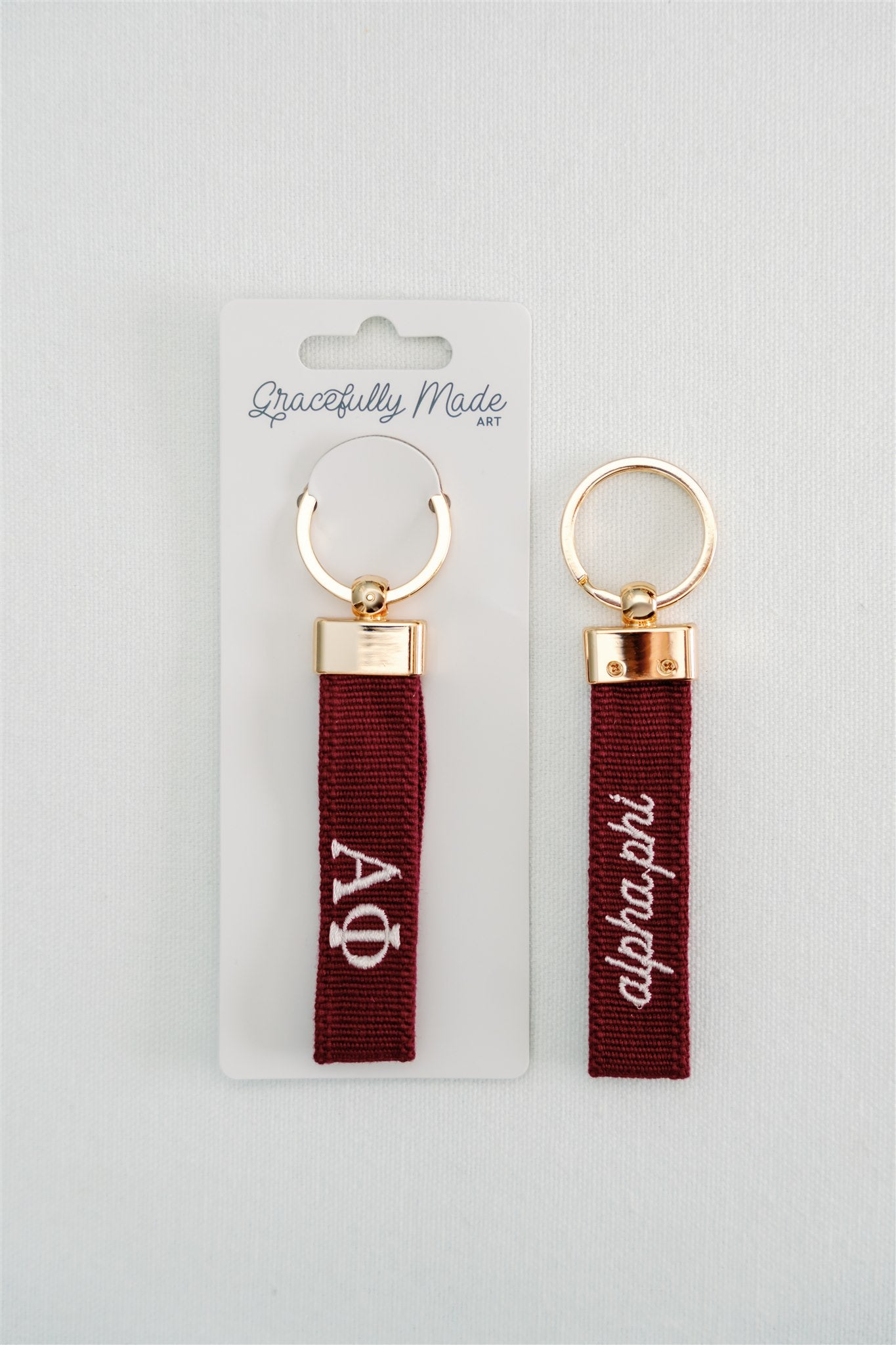Two red keychains with white Alpha Phi Greek letters and gold rings on a white background