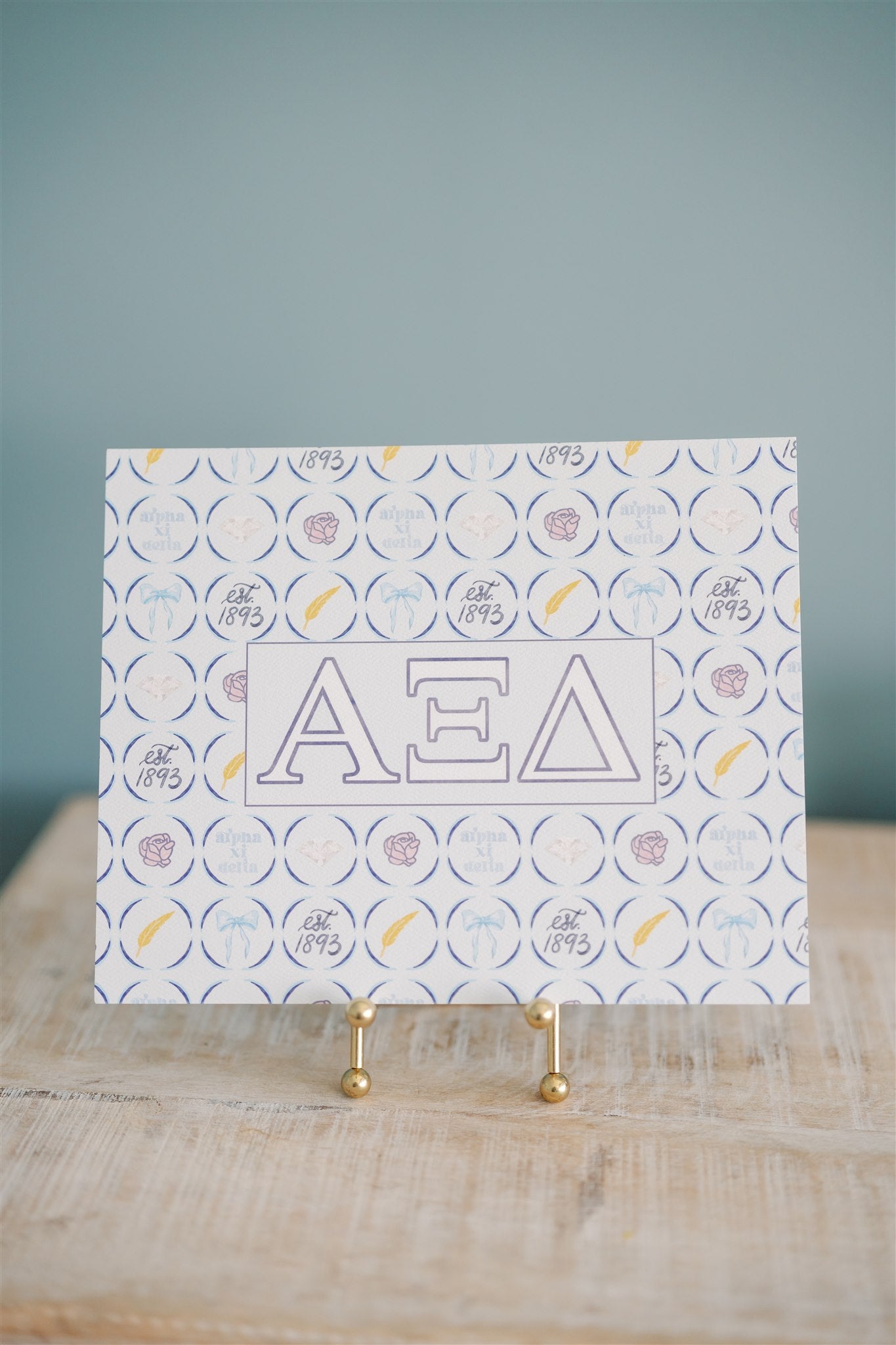 Art print with Alpha Xi Delta Greek letters on a stand against a blue background