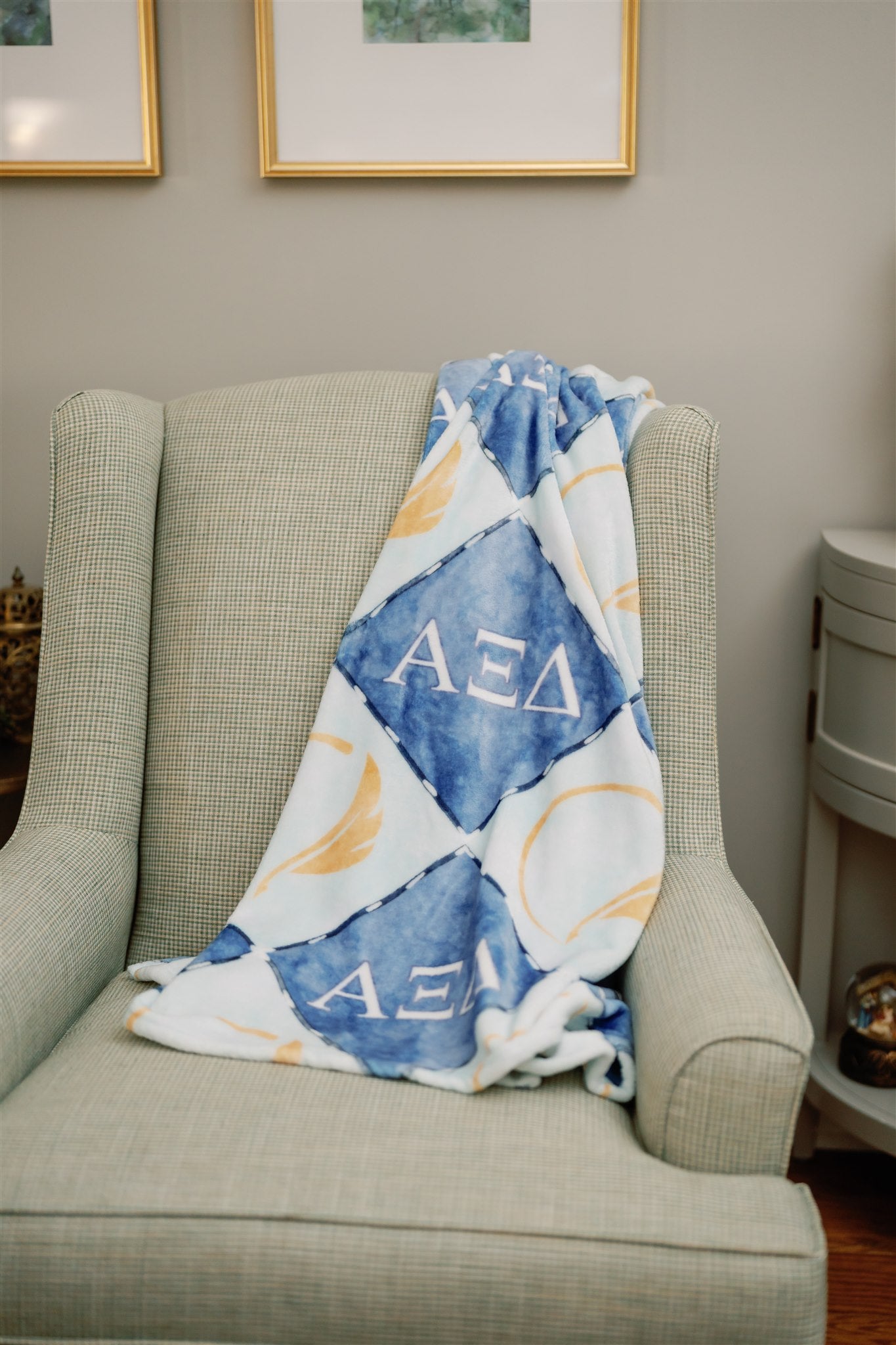 Blanket with 'Alpha Xi Delta' pattern draped over a chair in a room.