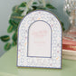 Decorative arch-shaped frame with Alpha Xi Delta pattern and Greek letters on a green surface.