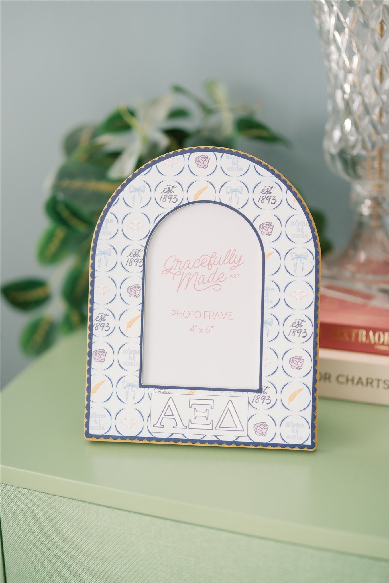 Decorative arch-shaped frame with Alpha Xi Delta pattern and Greek letters on a green surface.