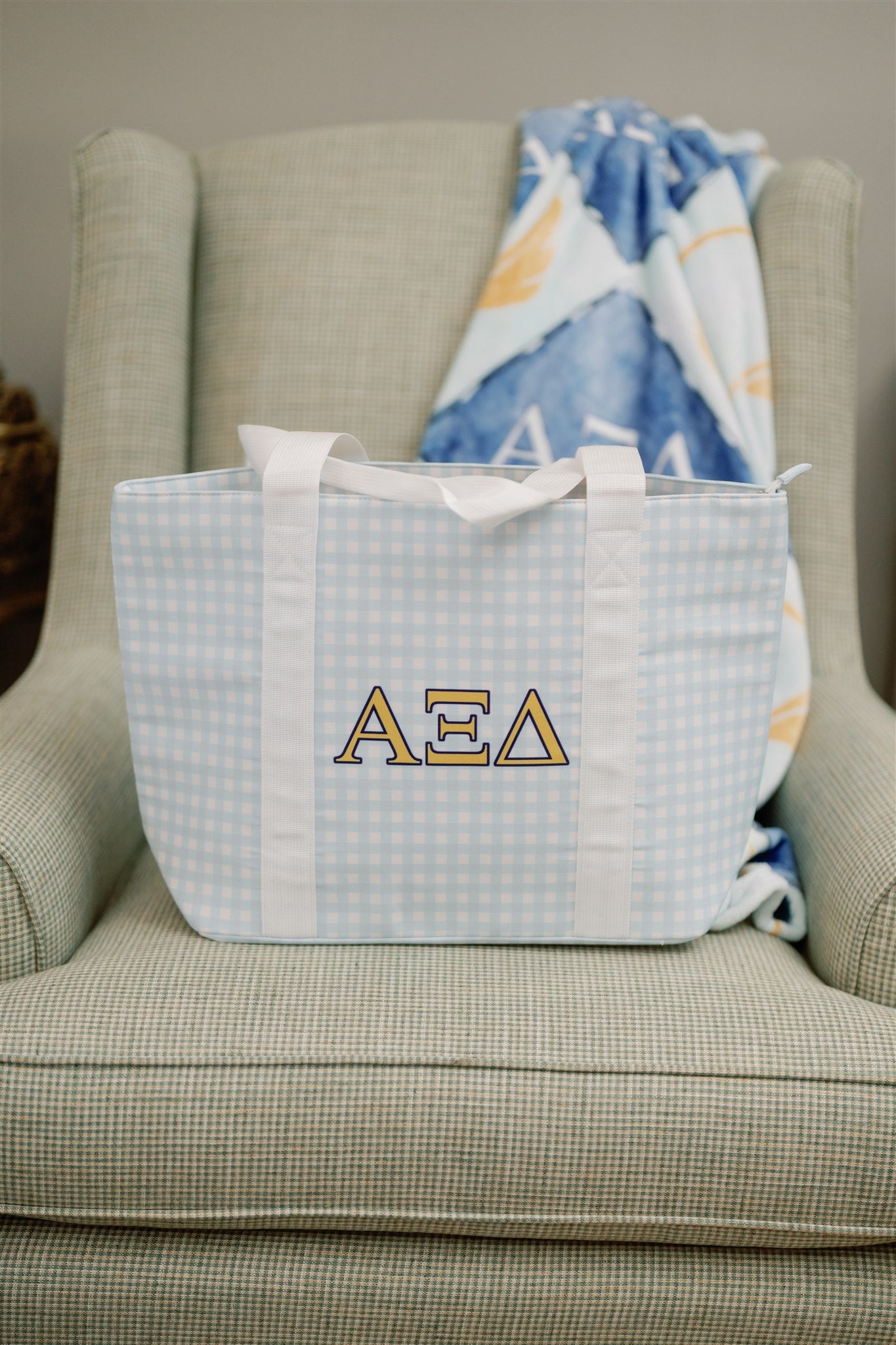 Light blue checkered tote bag with Alpha Xi Delta letters on a beige armchair