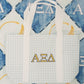 White and light blue checkered tote bag with Alpha Xi Delta letters on a patterned background