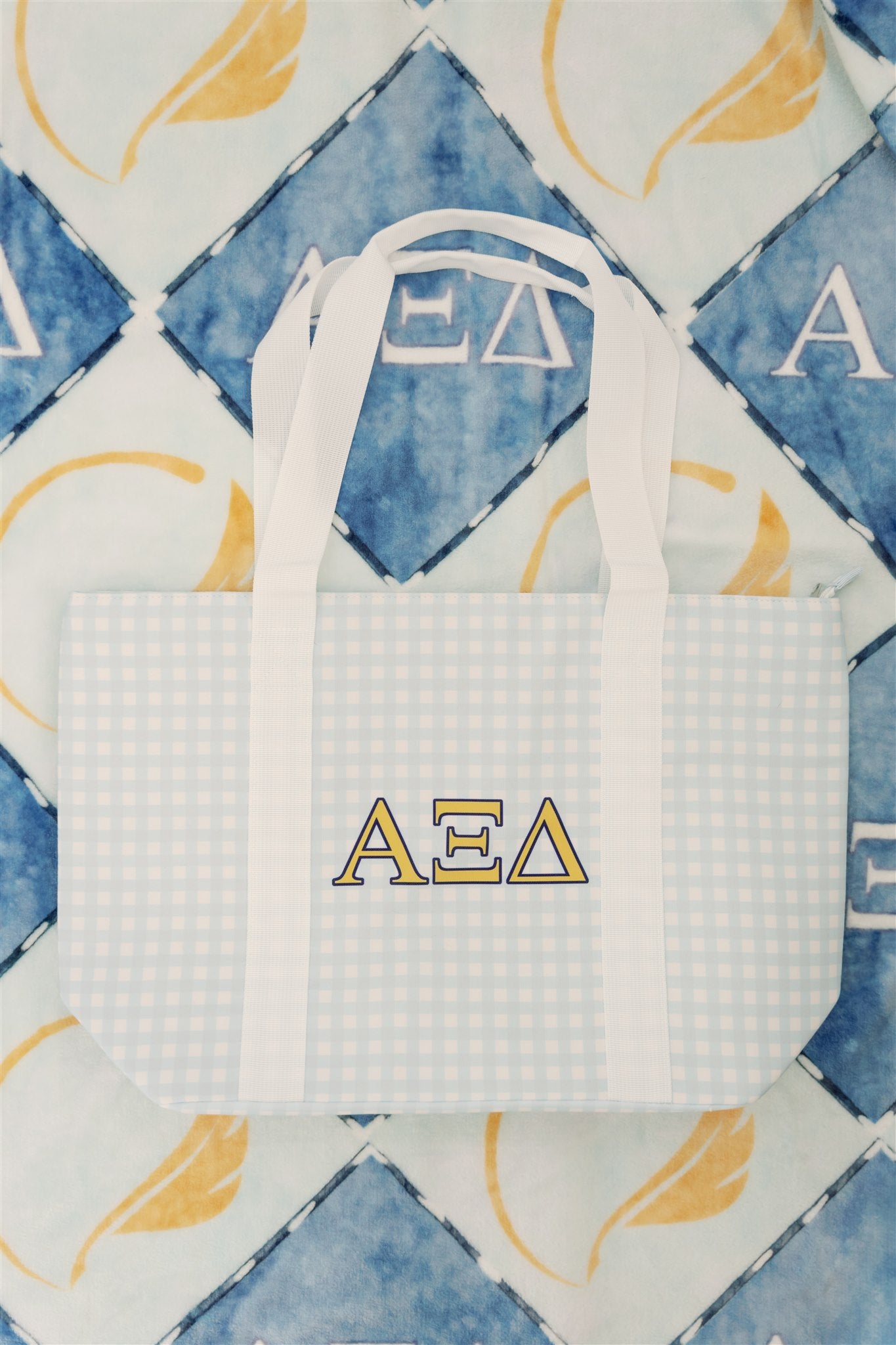 White and light blue checkered tote bag with Alpha Xi Delta letters on a patterned background