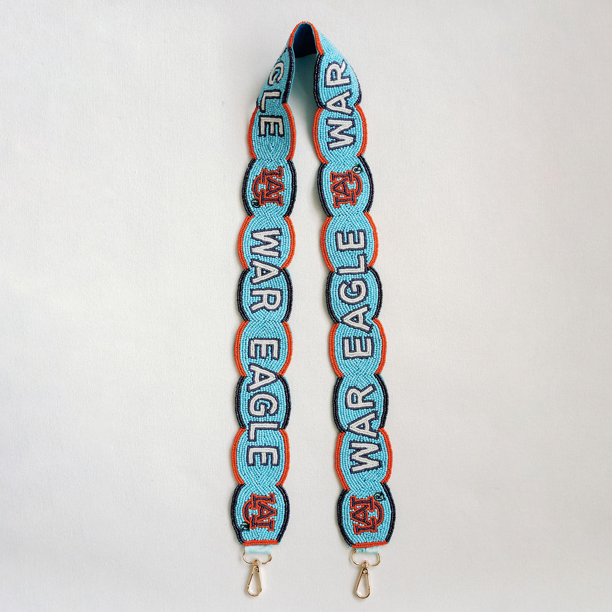 A light blue beaded strap featuring repeating 'WAR EAGLE' text in white outlined in navy blue, accented with orange details, a scalloped border, and finished with gold-tone metal clasps at the bottom.