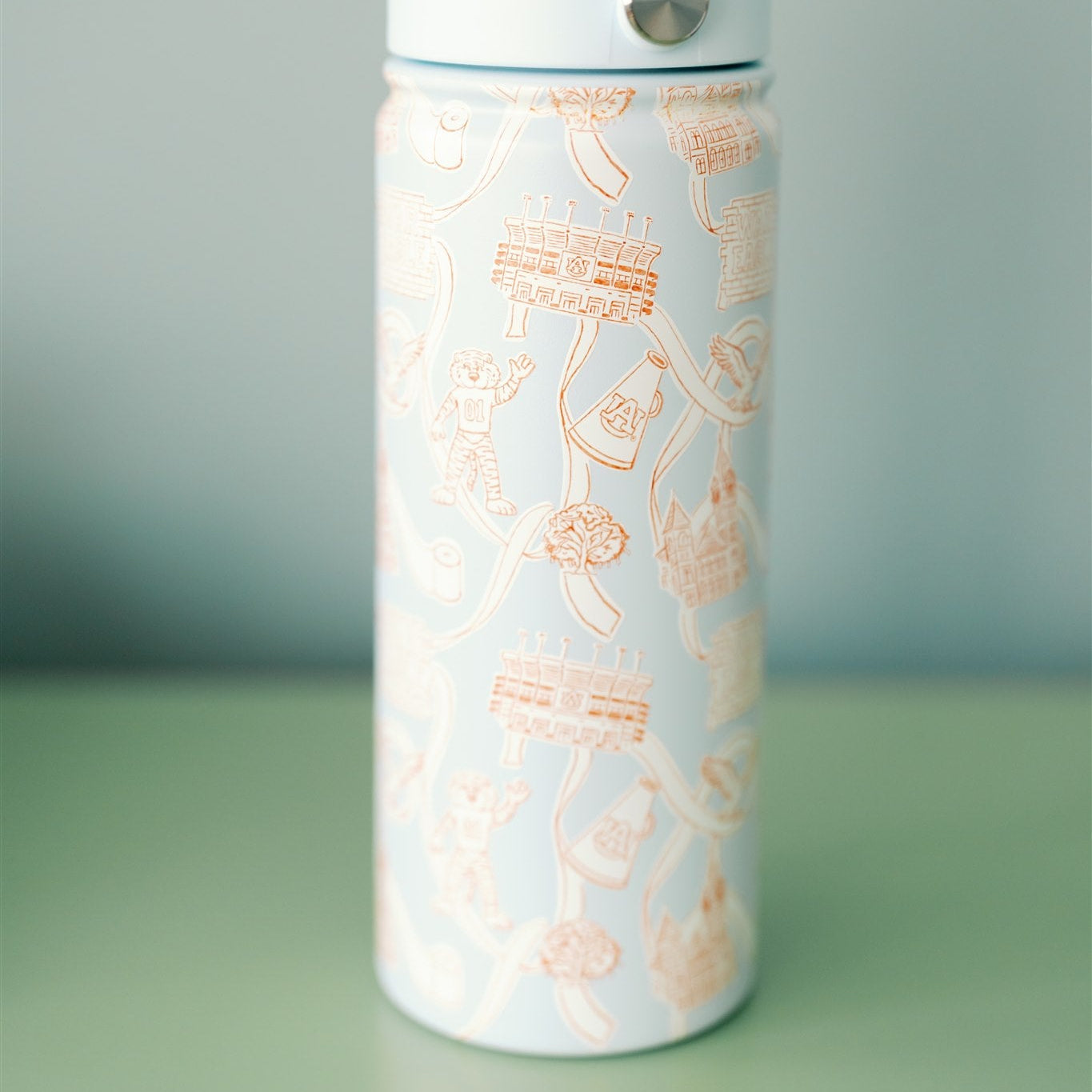 Light blue water bottle with white and orange Auburn designs on a green surface and gray background