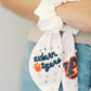White scrunchie with two ribbons featuring beading of the Auburn logo and "Auburn Tigers."