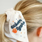 White scrunchie with two ribbons featuring beading of the Auburn logo and "Auburn Tigers."