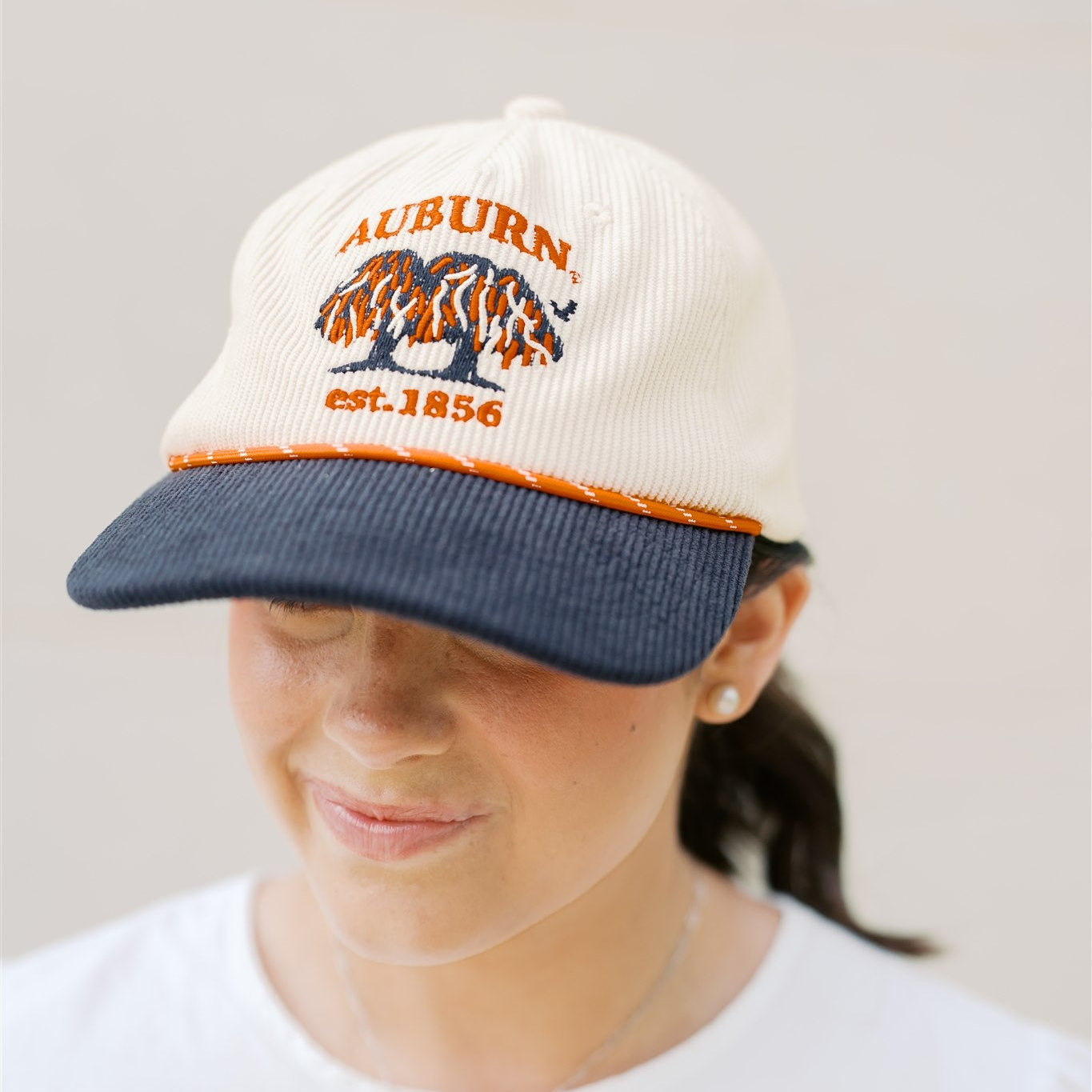 Person wearing a baseball cap with 'Auburn' text on a white cap with a navy blue brim.