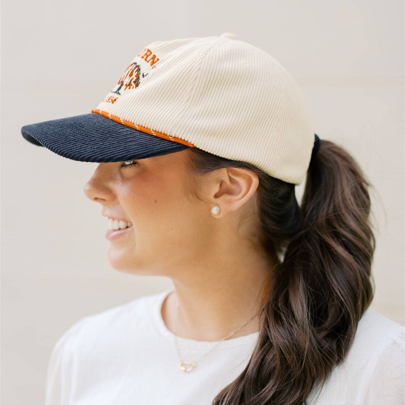 Woman wearing a beige and navy cap with a ponytail, against a plain background