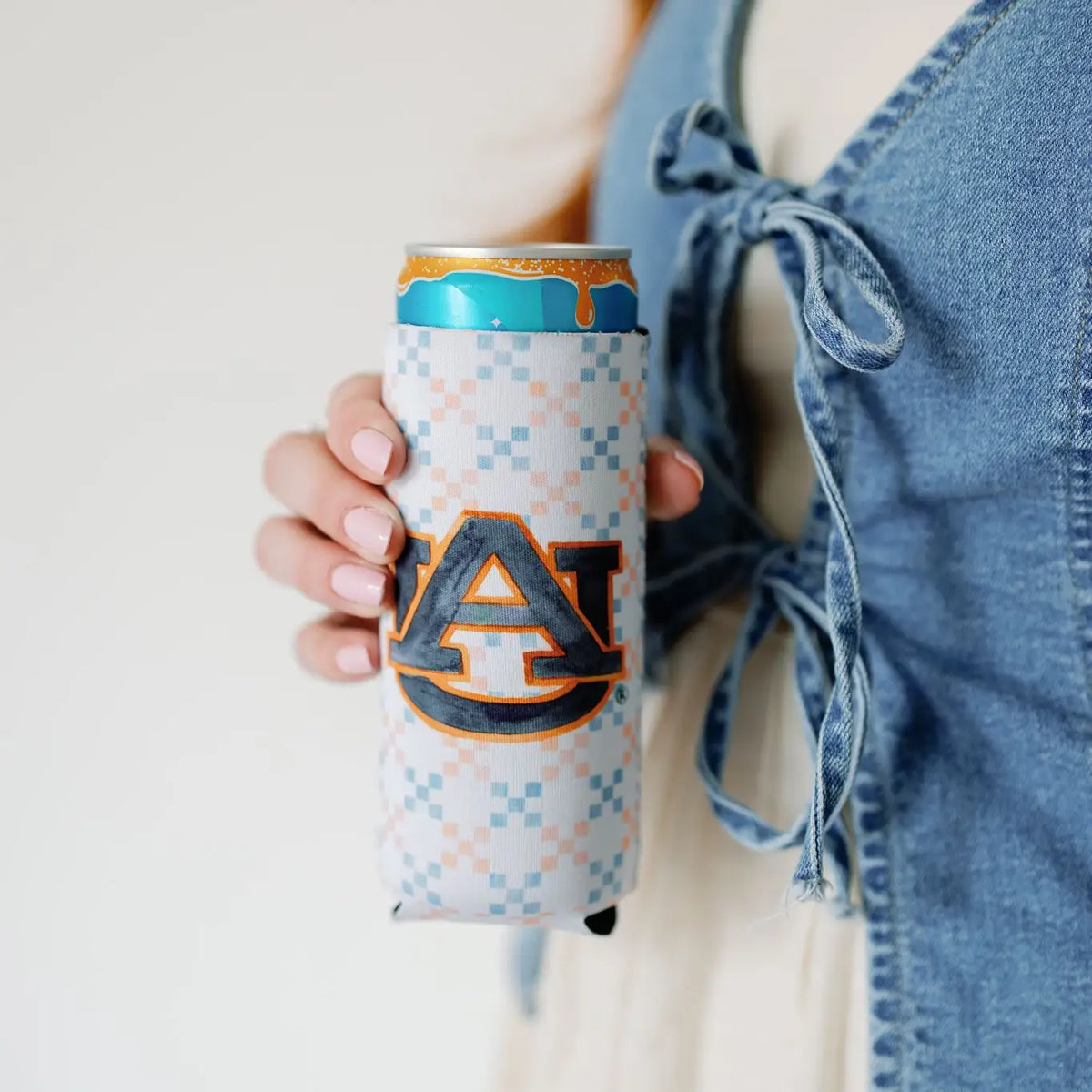 A person holding an aluminum can with a white, light blue, and orange patterned koozie featuring a large navy and orange 'AU' logo.