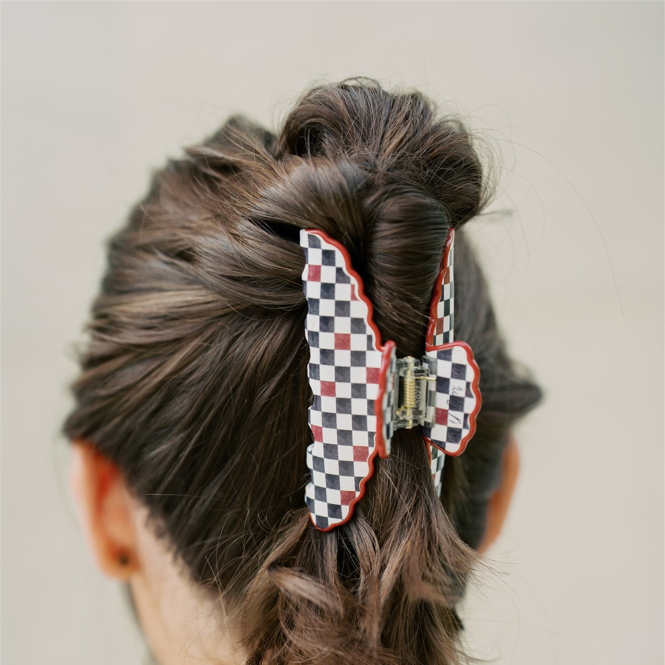 Person with a red and black checkered hair clip in their hair against a plain background