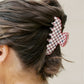 Person with hair styled using a red and black checkered hair clip on a plain background