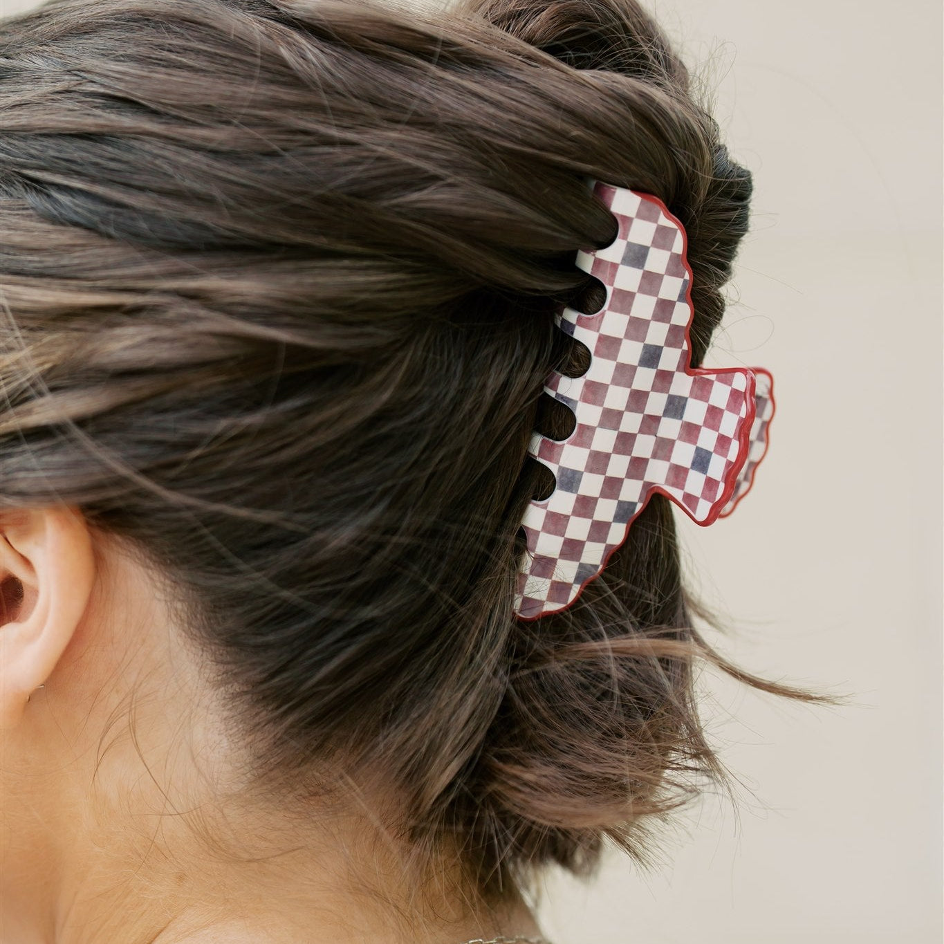 Person with hair styled using a red and black checkered hair clip on a plain background
