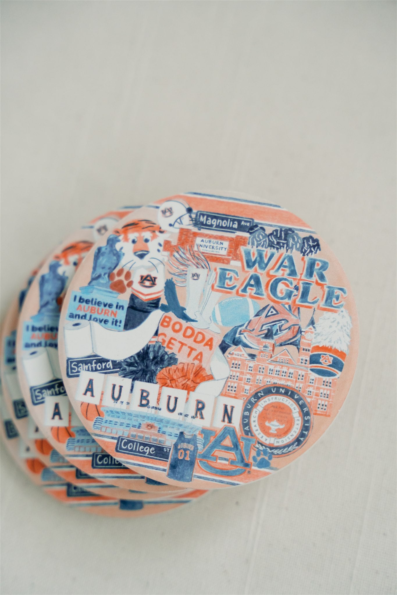 Ceramic coasters with a collage of watercolor illustrations of Auburn University landmarks and icons.