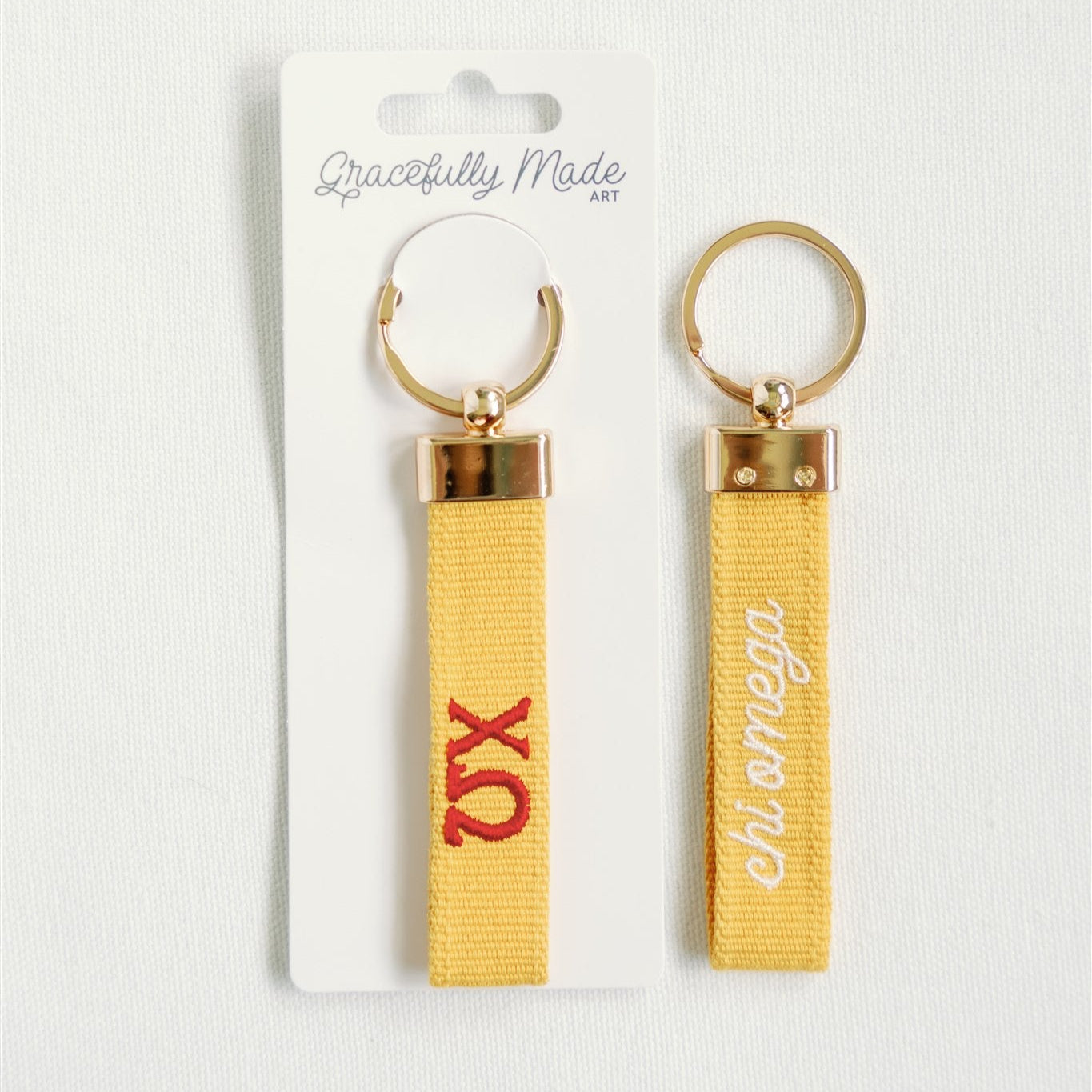 Two yellow keychains with gold rings on a white background, one with red Chi Omega Greek letters and the other with white  Chi Omega.