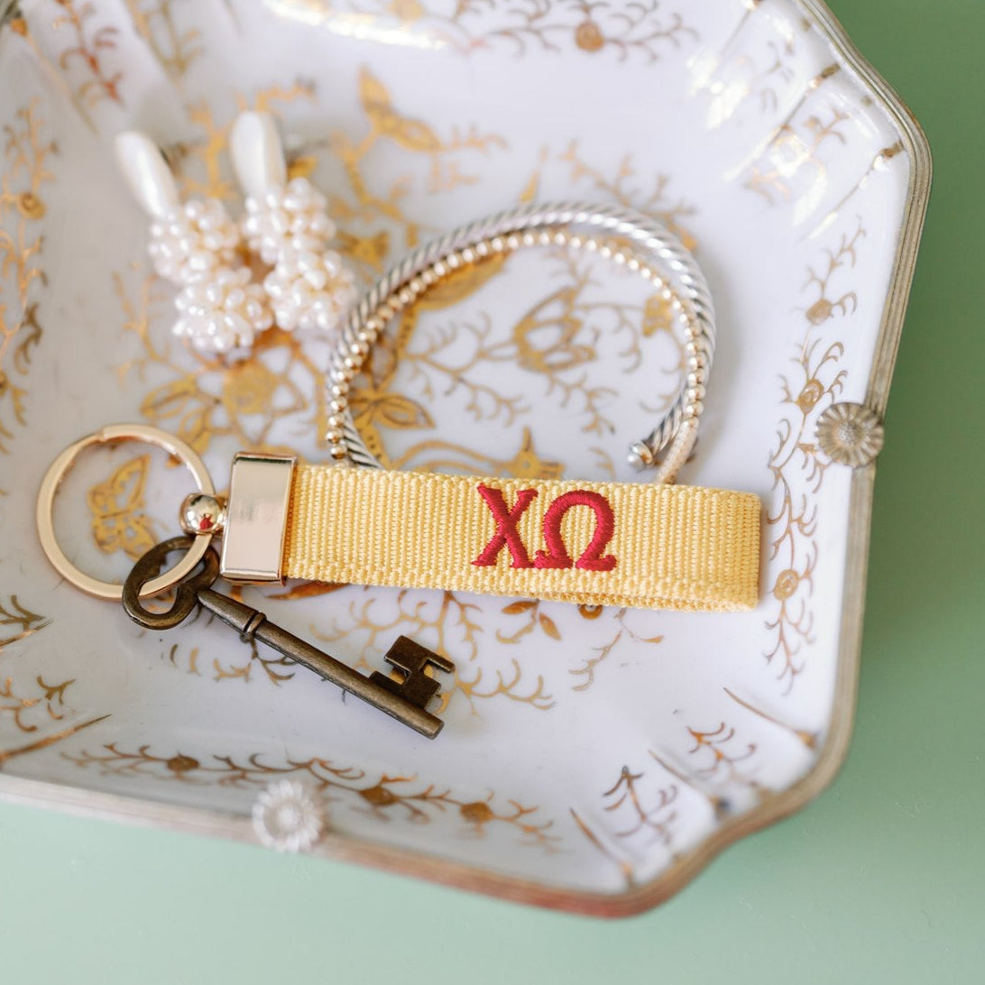 Decorative dish with jewelry and yellow keychain and red Chi Omega Greek letters embroidered on it