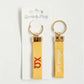 Front and back of the yellow Chi Omega keychain with Gracefully Made Art branded packaging.