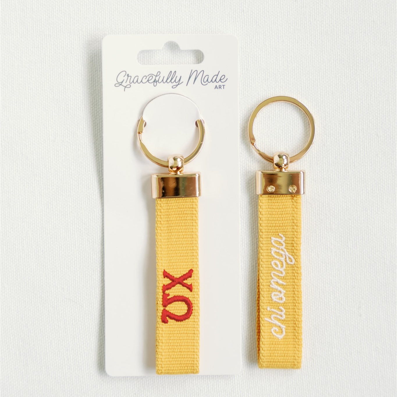 Front and back of the yellow Chi Omega keychain with Gracefully Made Art branded packaging.