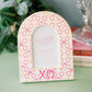 Decorative Chi Omega patterned photo frame on a surface with books and plants in the background.