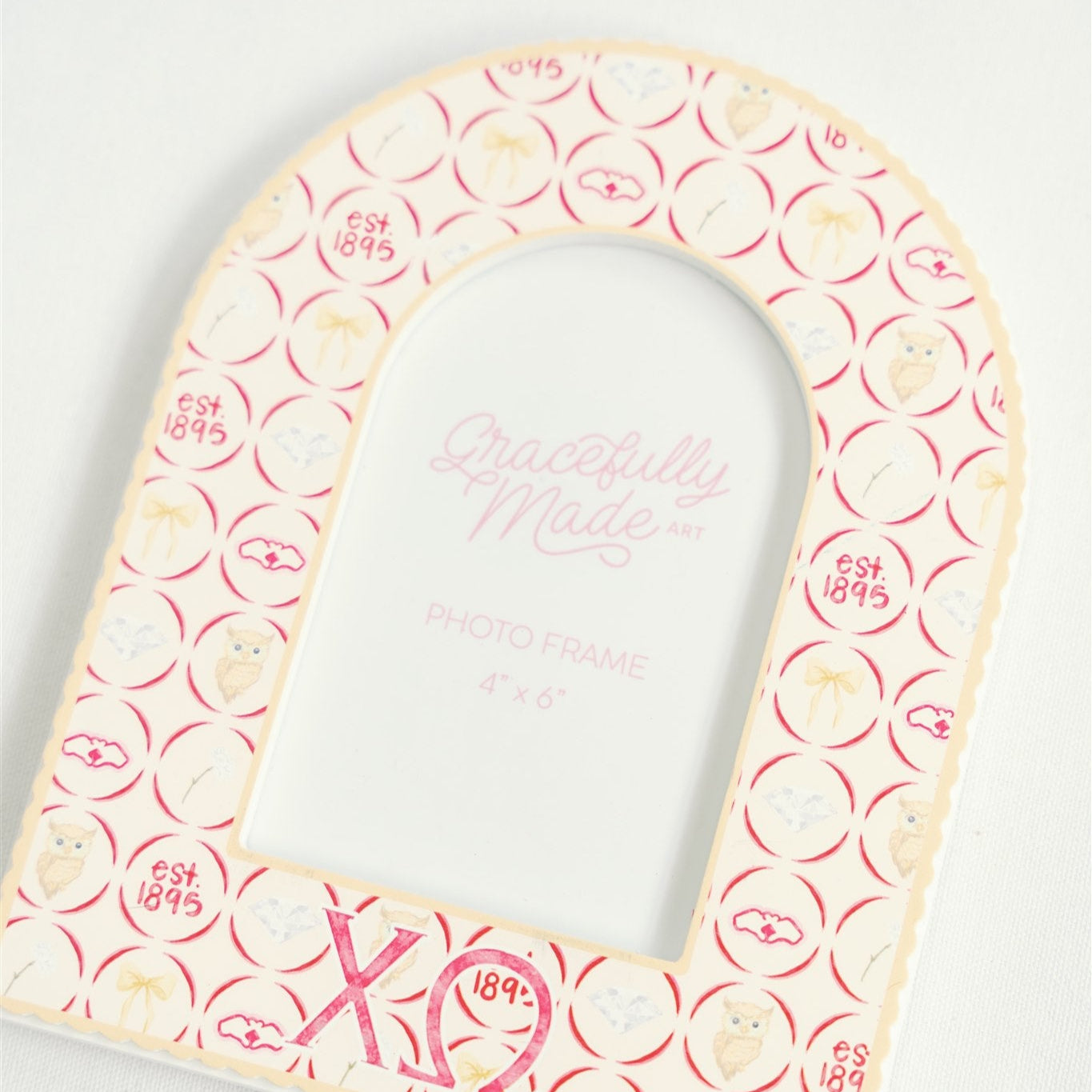 Close up of arched shaped picture frame with Chi Omega pattern and Greek letters on white background.
