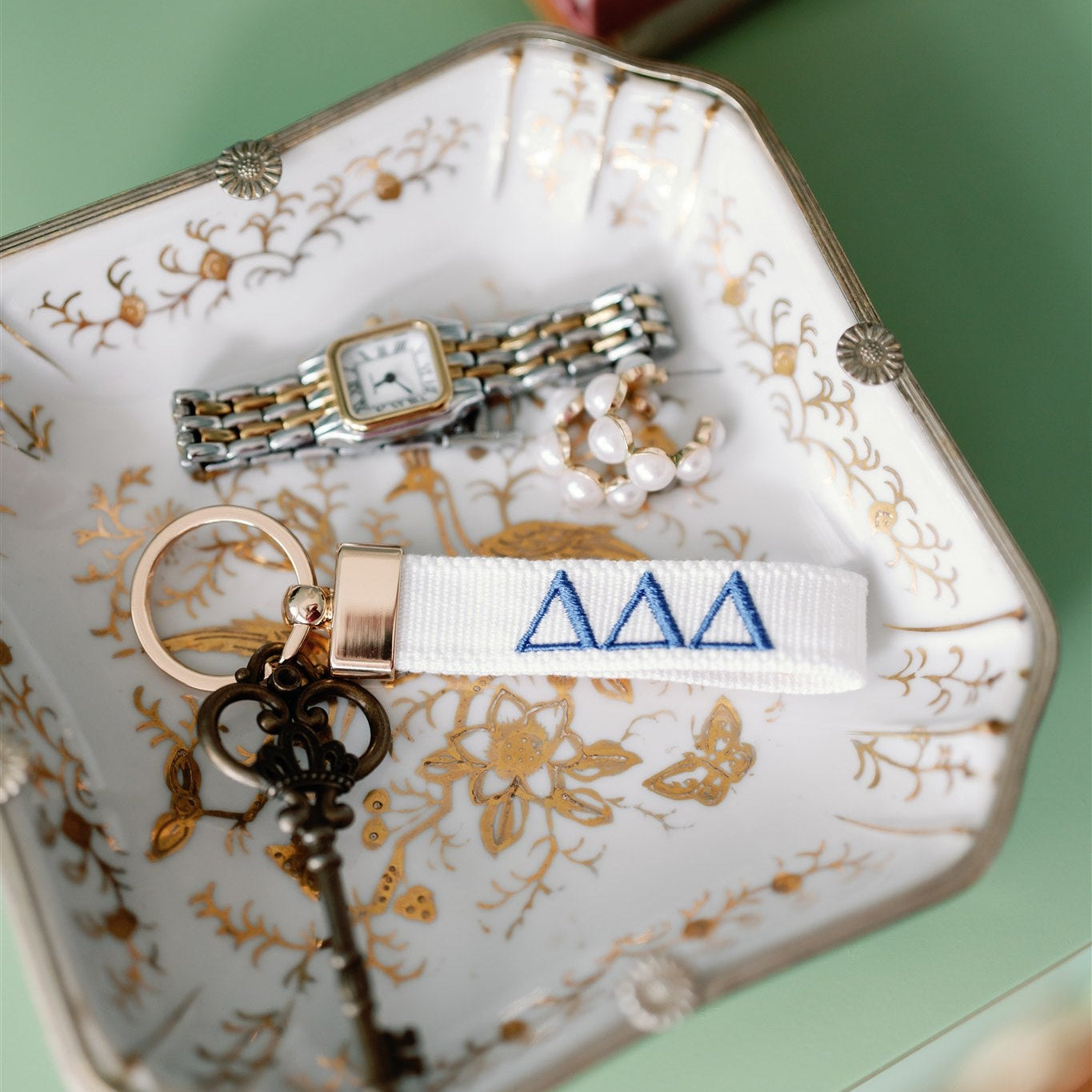 Decorative jewelry dish with jewelry and a white keychain with Tri Delta Greek letters embroidered on it