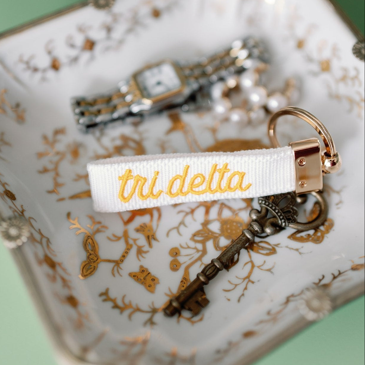 White keychain with yellow Tri Delta embroidered on it set on a decorative jewelry tray
