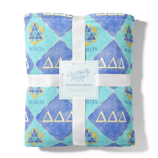Folded fleece blanket with geometric pattern and 'Tri Delta' text, branded 'Gracefully Made Art'.