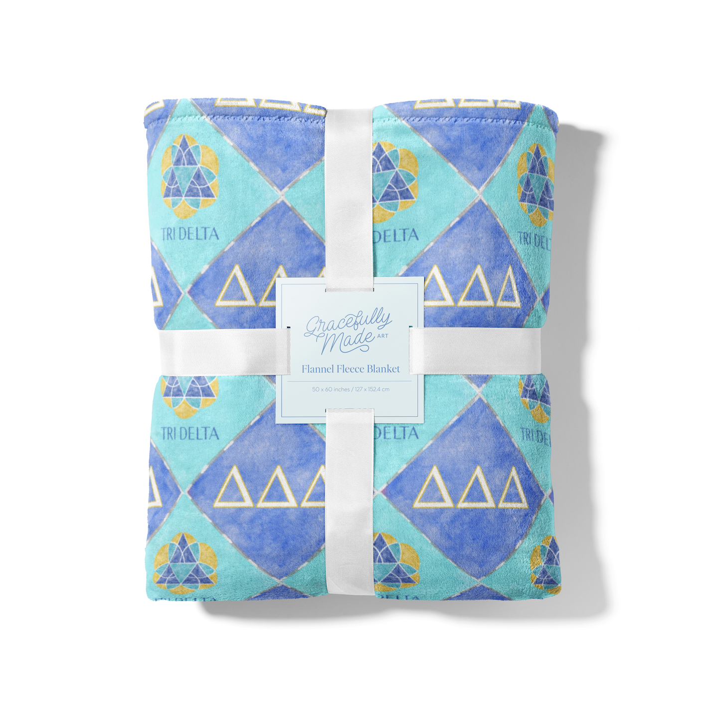 Packaged blanket with blue and green Tri Delta geometric pattern and white ribbon on a white background