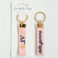 Two pink keychains with gold accents and Delta Gamma Greek letters on a white background