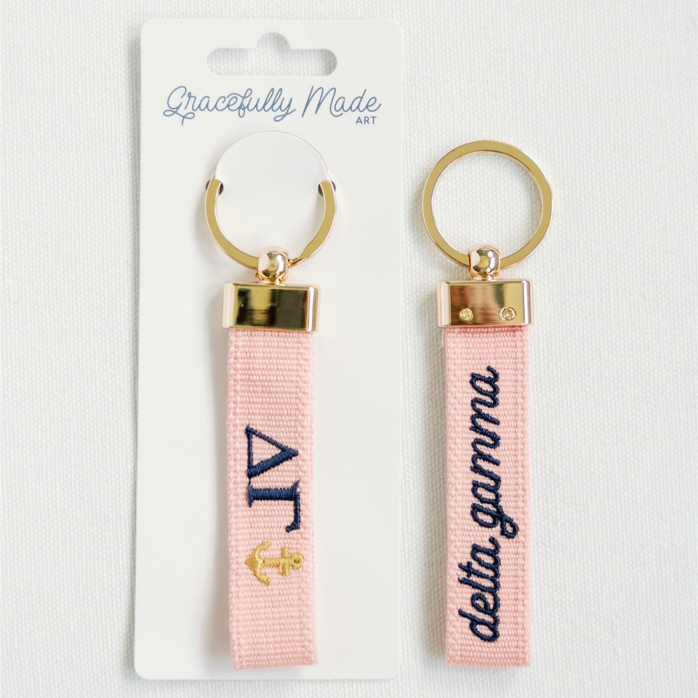 Two pink keychains with gold accents and Delta Gamma Greek letters on a white background