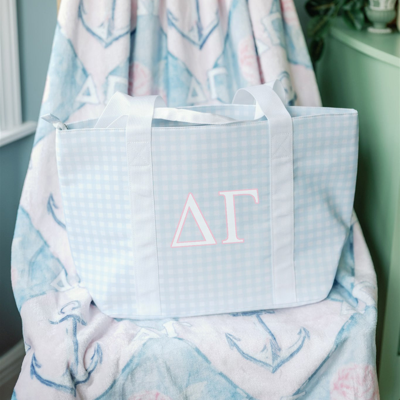 Light blue tote bag with pink Delta Gamma Greek letters on a patterned chair