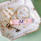 Pink keychain with Delta Gamma Greek letters and an anchor embroidered on it set on a jewelry dish.