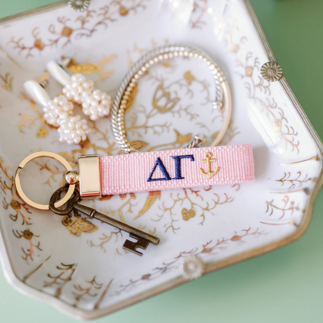 Pink keychain with Delta Gamma Greek letters and an anchor embroidered on it set on a jewelry dish.