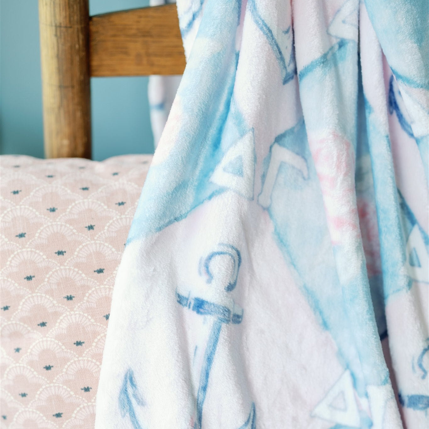 Light blue and pink patterned blanket draped over a wooden chair against a light blue wall