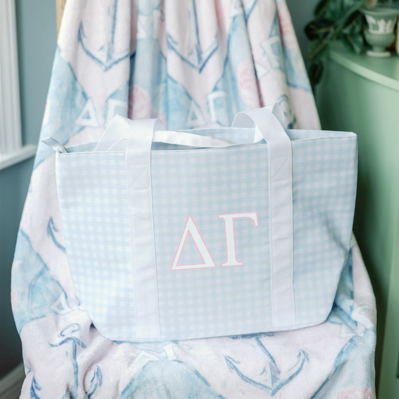 Light blue checkered tote bag with pink Delta Gamma Greek letters on a patterned chair