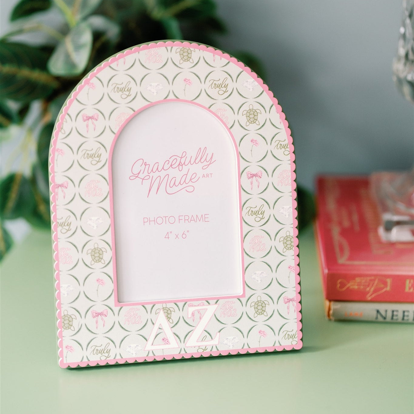 Decorative photo frame with pink and green design and Delta Zeta Greek letters sitting on a green dresser.