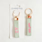 Front and back of a light green keychain with Delta Zeta Greek letters embroidered in pink.