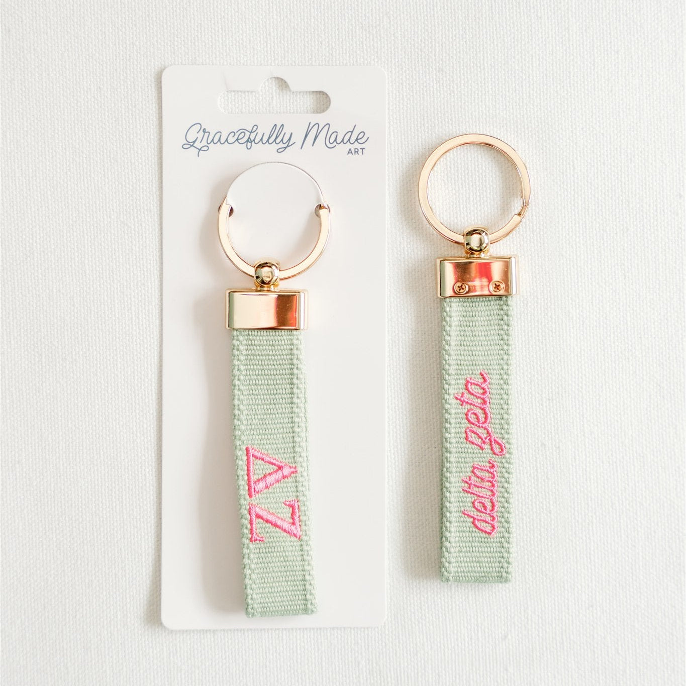 Front and back of a light green keychain with Delta Zeta Greek letters embroidered in pink.