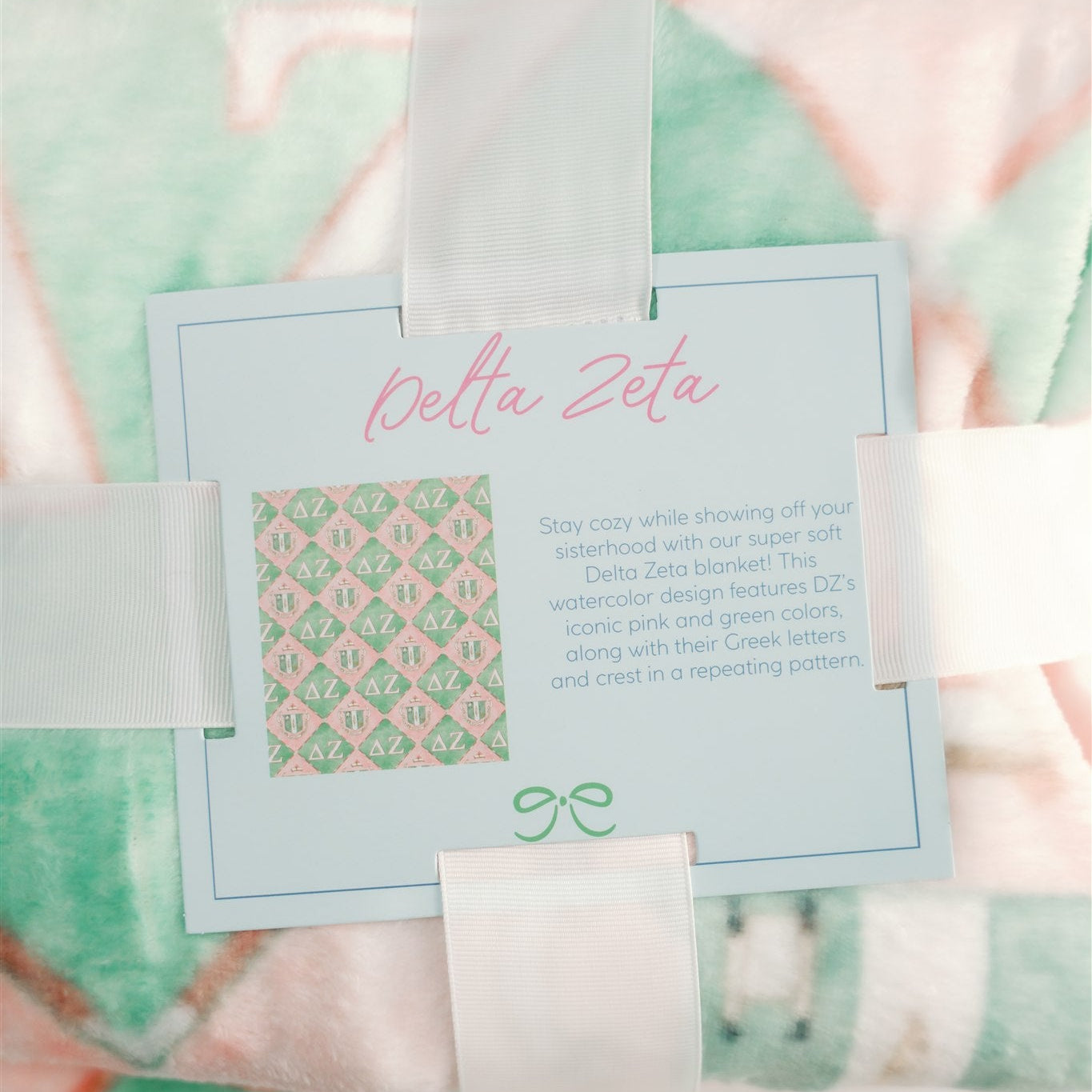 Delta Zeta branded product packaging with a blanket and card on a patterned background