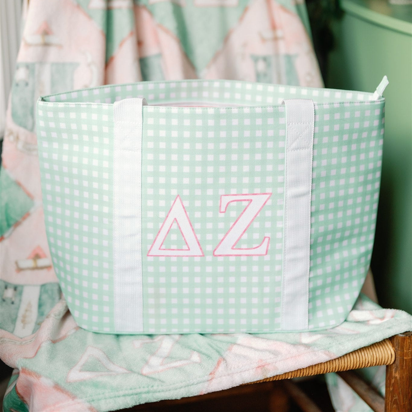 Green checkered tote bag with pink 'Delta Zeta' letters propped on a chair.
