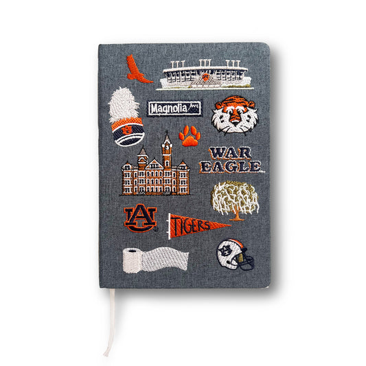 Hardcover navy blue notebook with various Auburn University icons embroidered on the front.